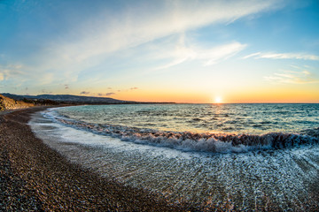View of the beautiful sunset over the sea with wild pebble beach coast. Fisheye effect