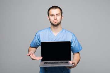 Portrait of a happy male doctor dressed in uniform with stethoscope showing blank screen laptop computer isolated over gray background