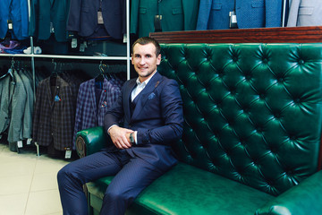 stylish man sits store costumes on a green leather sofa