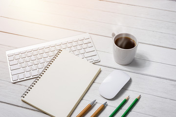 Wooden White office desk table with cup of coffee, Notebook, Pen on it.