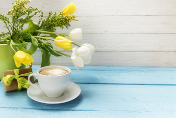 coffee cup, yellow and white tulip flowers in a green vase and a little gift on turquoise wood,...