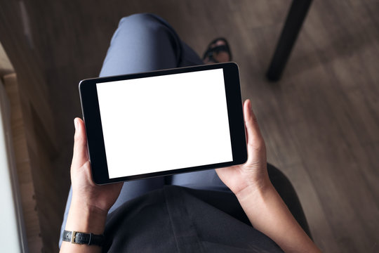 Top view mockup image of a woman sitting cross legged and holding black tablet pc with blank white desktop screen