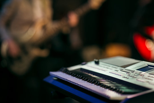 Electronic musical keyboard synthesizer on stage, close up. Blurred abstract bokeh background with guitar player
