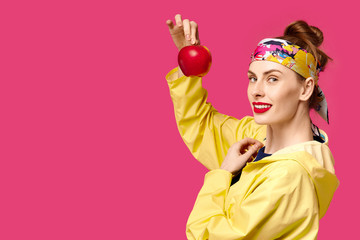 Young woman on a pink background and a yellow coat holds an apple in her hands. Concept of healthy nutrition and sports.  Colour obsession concept.  Minimalistic style. Stylish Trendy