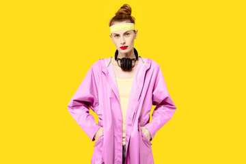 Young woman on a yellow background and a pink coat hugs music worm wireless headphones. Colour obsession concept.  Minimalistic style. Stylish Trendy