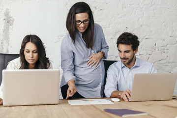 Young pregnant woman at work with his associates in the office while tells them what to do