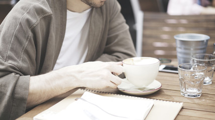 A white man is holding a cup of coffee in a white beige cup of cafe outdoors