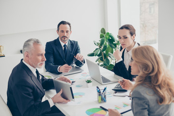 Handsome, aged, senior with grey hair showing presentation to his minded ponder colleagues using tablet, four business persons together sitting in work place, station at desk