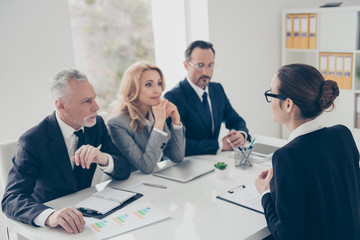 Portrait of young attractive woman in glasses having job interview with three stylish business persons in financial company, sitting in work place, station, telling about her experience