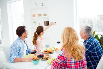 Brunette women shooting photo on smart phone with her relatives, guests, visitors in house, apartment, room, festive couples sitting at the table, eating food, drinking wine, domestic lifestyle
