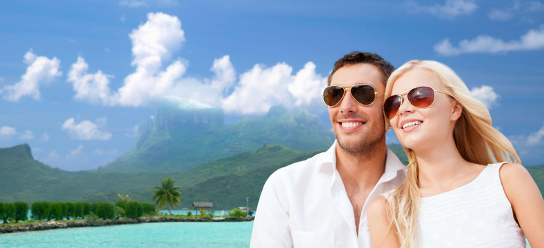 travel, tourism and summer holidays concept - happy couple in sunglasses at touristic resort over exotic bora bora island background