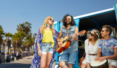 summer holidays, road trip, travel and vacation concept - happy young hippie friends having fun and playing music over minivan car and venice beach in los angeles background