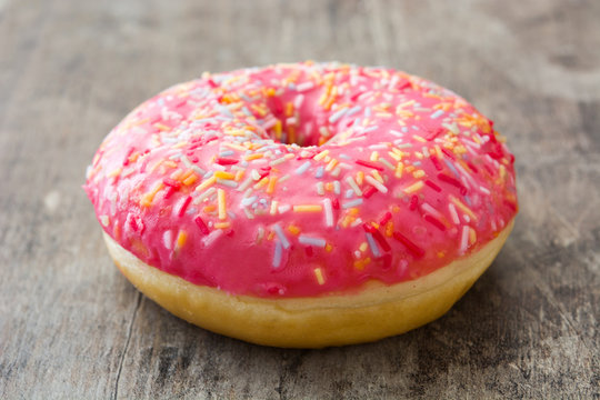 Pink frosted donut with colorful sprinkles on wooden table