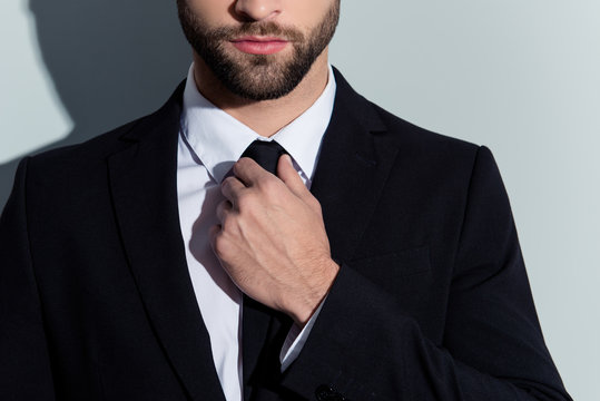 Close up cropped portrait of half face serious man in classy outfit with bristle, holding hand on tie, preparing for event, isolated on grey background