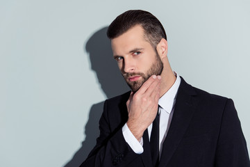 Portrait of thoughtful, virile, harsh, manly, stunning guy in classic outfit touching his beard, suspects something, holding hand on chin, isolated on grey background