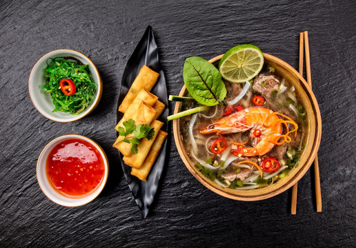 Asian shrimps soup with spring rolls and chopsticks.