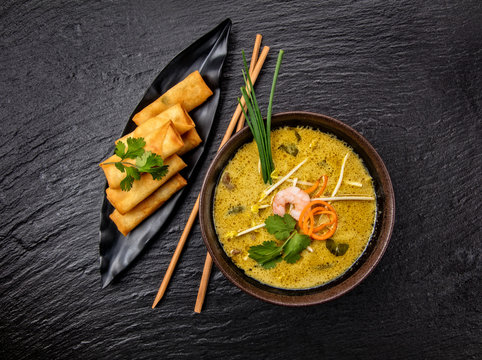 Asian kari soup with spring rolls and chopsticks.