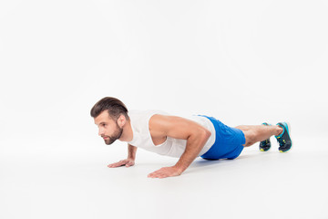 Side view full body portrait of concentrated, confident, sporty, athletic, attractive, professional, successful man making, showing push up position, isolated on white background