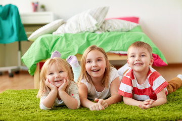 childhood, leisure and family concept - happy little kids lying on floor or carpet