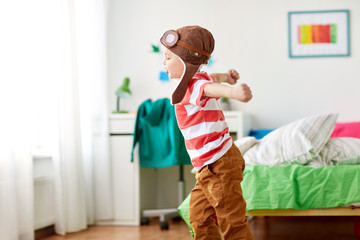childhood, imagination and dream concept - happy little boy in pilot hat playing game at home © Syda Productions