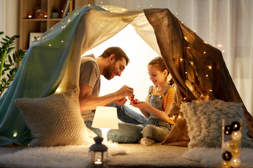 family, hygge and people concept - happy father and little daughter playing tea party in kids tent...