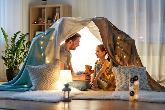 Family, Hygge And People Concept - Happy Father With Teddy Bear Toy And Little Daughter Playing In Kids Tent At Night At Home