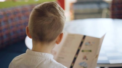Handsome young boy reading menu in cafe. 4K