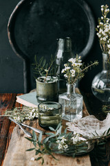 Spring flowers and greens in the decor on the table, in glass bottles with water and droplets on the glass. Warm gamma and restrained composition, with small flowers and grass