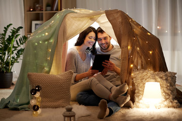 leisure, hygge, technology and people concept - happy couple with tablet pc computer in kids tent at home © Syda Productions