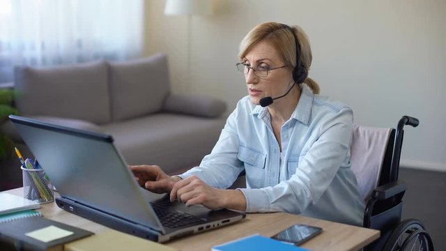 Disabled female manager sitting at office desk, working on laptop from home