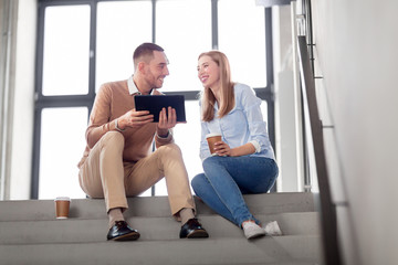 Fototapeta na wymiar business people, technology and corporate concept -smiling man and woman with tablet pc and coffee at office stairs