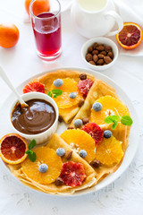 French pancakes. Crepe Suzette with caramel, oranges, blueberries, almonds and hazelnuts on white table cloth