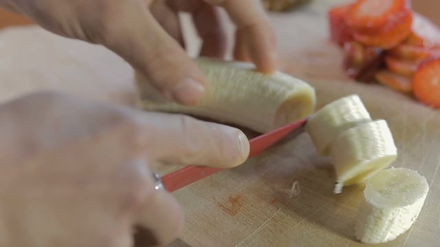 Mano di un uomo che tagliano la banana con un coltello rosso su un tagliere di legno
