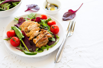 Sliced grilled chicken with green leaves salad on white plate