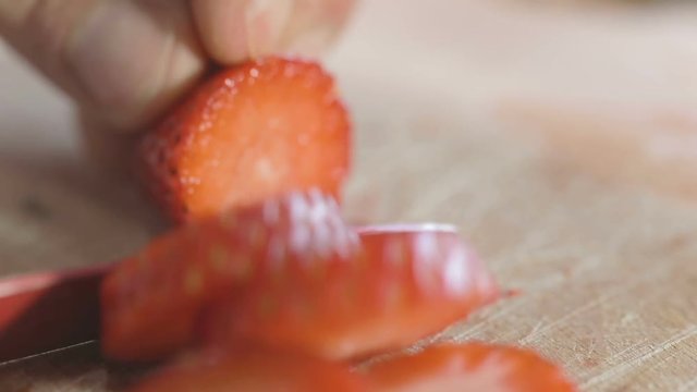 Mano di un uomo che tagliano la fragola con un coltello rosso su un tagliere di legno