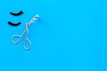 Curled and thick eyelashes. False eyelashes and eyelash curler on blue background top view copy space