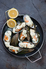Above view of baked kiwi mussels with cheese sauce and lemon served in a metal pan, cracked asphalt background, vertical shot