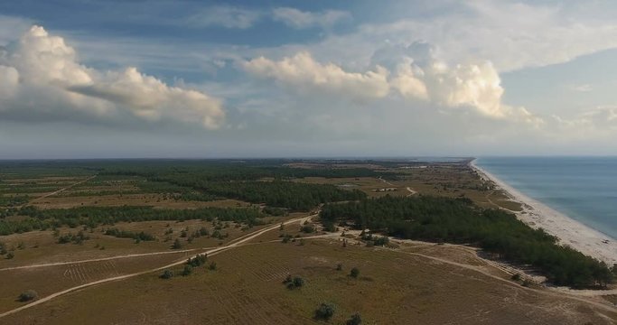 Aerial view, Flight over forest and dirt road along fantastic seacoast against blue clouds, kinburn foreland
