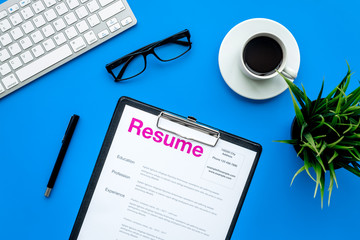 Empoyment concept. Resume on blue work desk with coffee, glasses, keyboard top view