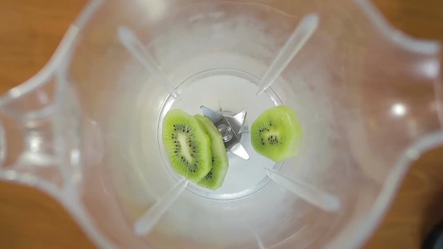 Uomo sta versando la frutta fresca dentro un frullatore per il frullato a colazione. kiwi, banana, fragole, mango.