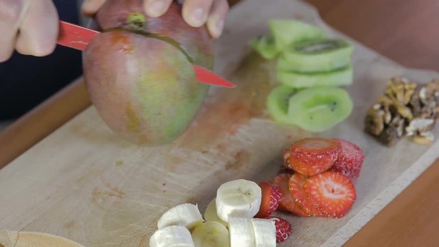 Mano di un uomo che tagliano il mango con un coltello rosso su un tagliere di legno