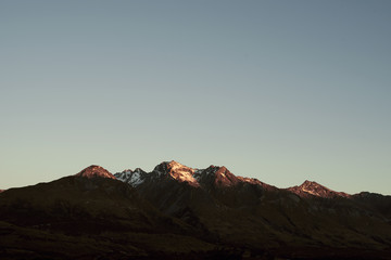Paisaje de picos de montañas nevadas con cielo azul despejado al atardecer en Nueva Zelanda	