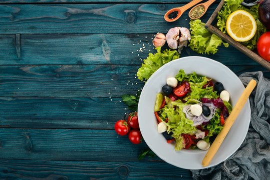 Salad with mozzarella and fresh vegetables. On a blue wooden background. Top view. Copy space for your text.