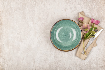 Empty green plate, cutlery set with vintage style linen napkin and purple flowers on stone background. Top view, flat lay and copy space
