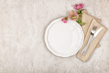 Empty white plate, cutlery set with vintage style linen napkin and purple flowers on stone background. Top view, flat lay and copy space
