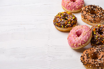 Delicious donuts with multicolored glaze and topping on wooden background