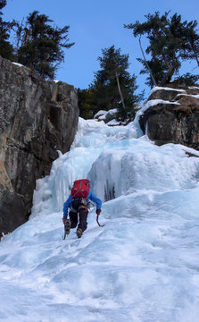 male ice climber in a blue jacket on a gorgrous frozen waterfall climbing in the Alps in deep winter