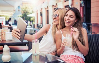 Friends meeting in a cafe. Young women drinking lemonade and have fun with tablet. Consumerism, lifestyle concept
