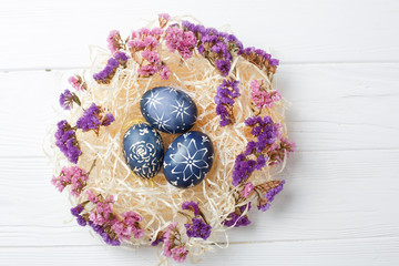 Dark blue easter eggs in nest on white wooden background