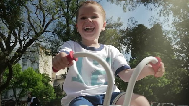 Little boy riding a tricycle at the park, playground. Slow Motion. Day. Happy